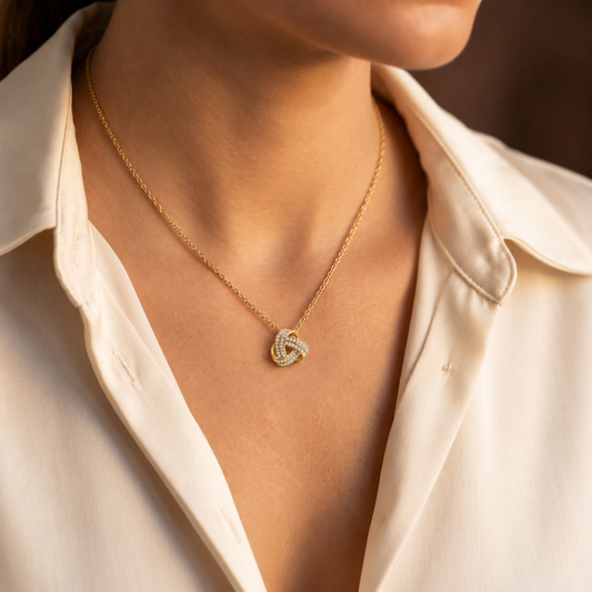Woman wearing a gold love knot necklace with an ivory blouse