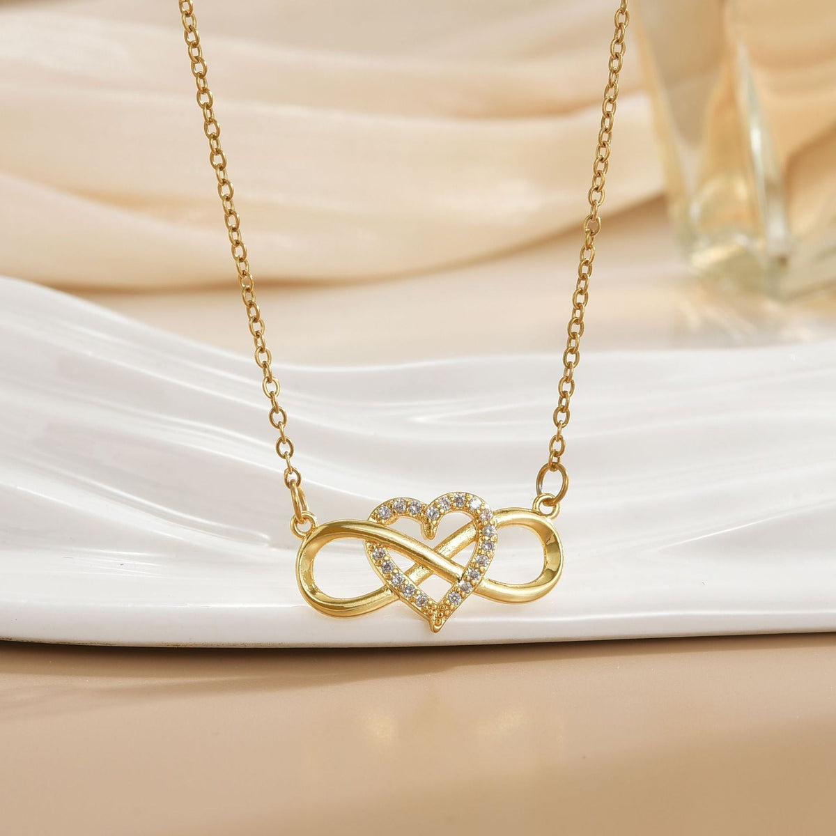 Gold infinity heart pendant on a cream fabric background