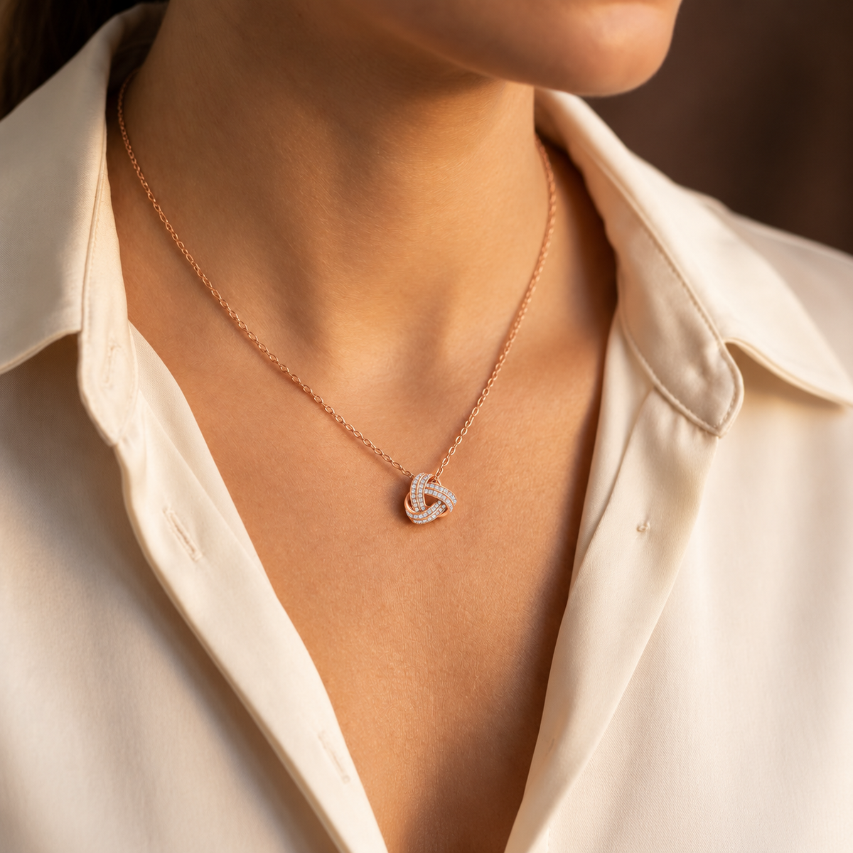Woman wearing a rose gold love knot necklace with an ivory blouse
