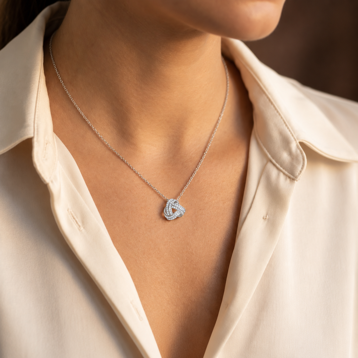 Woman wearing a silver love knot necklace with an ivory blouse